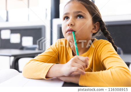 In school, in classroom, young biracial girl holding a pencil, looking thoughtful In school, in classroom, young biracial girl holding a pencil, looking thoughtful 116308915