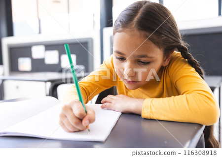 In school, young biracial girl with light brown skin focusing on writing in the classroom 116308918