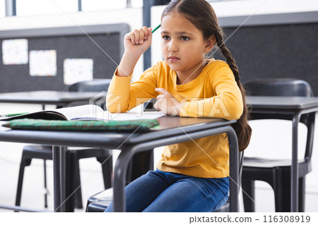 In school, young biracial girl sitting at a desk in a classroom, looking thoughtful In school, young biracial girl sitting at a desk in a classroom, looking thoughtful 116308919