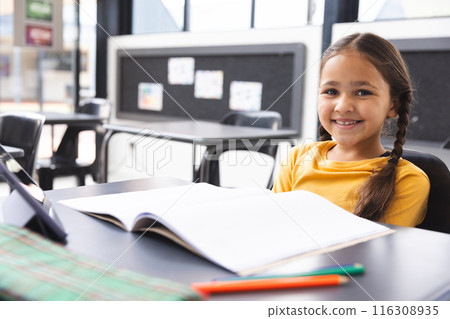 In school, in classroom, young biracial girl with a bright smile sitting at a desk with copy space In school, in classroom, young biracial girl with a bright smile sitting at a desk with copy space 116308935