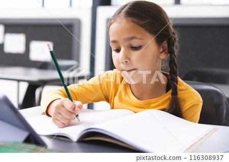 In school, young biracial girl with braided hair focusing on writing in the classroom In school, young biracial girl with braided hair focusing on writing in the classroom 116308937
