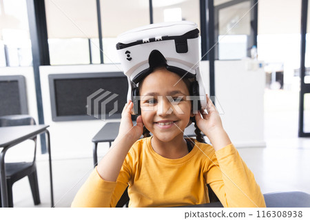 In school, in the classroom, a young biracial girl wearing a VR headset is smiling 116308938