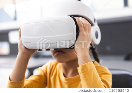 In school, young biracial girl wearing virtual reality headset, exploring in the classroom In school, young biracial girl wearing virtual reality headset, exploring in the classroom 116308940