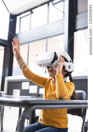 In school, young biracial girl wearing virtual reality headset raising hand in the classroom 116308941