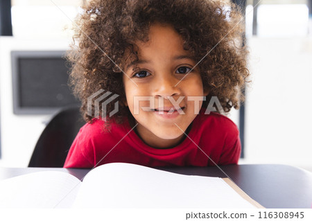 In school, young biracial male student wearing a red shirt reading a book in the classroom 116308945