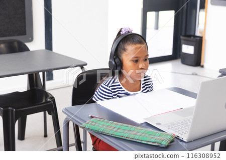 In school, young biracial female student wearing headphones focusing on a laptop in the classroom 116308952