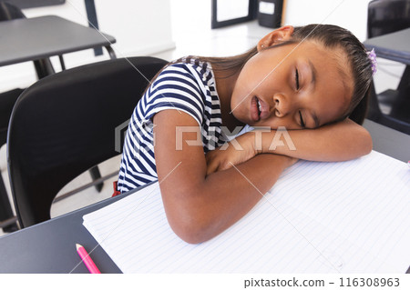 In school, young biracial girl with light brown skin is sleeping at her desk in the classroom In school, young biracial girl with light brown skin is sleeping at her desk in the classroom 116308963