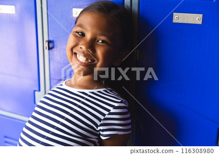 In school, young biracial girl with a bright smile standing by blue lockers In school, young biracial girl with a bright smile standing by blue lockers 116308980