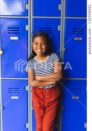 In school, young biracial female student leaning against blue lockers, smiling In school, young biracial female student leaning against blue lockers, smiling 116308981