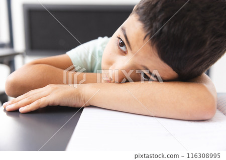In school, in classroom, biracial young boy leaning on a desk, looking bored In school, in classroom, biracial young boy leaning on a desk, looking bored 116308995