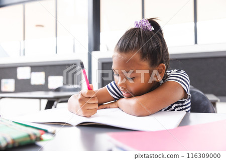 In school, in the classroom, young biracial girl focusing on writing in her notebook In school, in the classroom, young biracial girl focusing on writing in her notebook 116309000