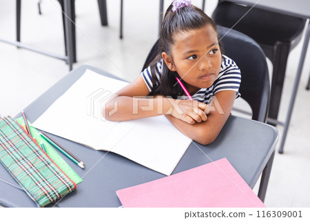 In school, young biracial girl sitting at a desk in a classroom, looking thoughtful In school, young biracial girl sitting at a desk in a classroom, looking thoughtful 116309001