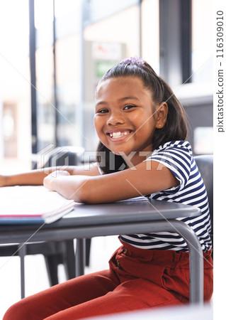 In school, young biracial girl with a bright smile sitting at a desk in a classroom In school, young biracial girl with a bright smile sitting at a desk in a classroom 116309010
