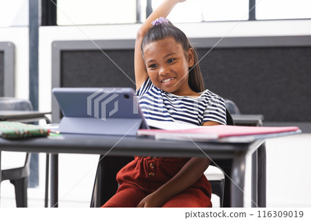 In school, young biracial girl sitting at desk in classroom, looking at tablet In school, young biracial girl sitting at desk in classroom, looking at tablet 116309019