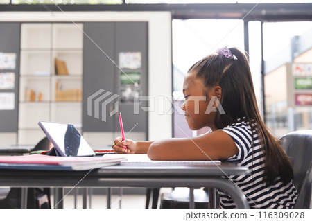 In school, young biracial girl focusing on her tablet in the classroom with copy space 116309028