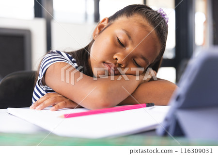 In school, in the classroom, a young biracial girl with light brown skin is sleeping on her desk 116309031