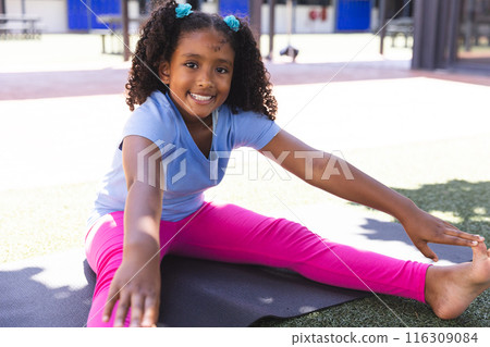 Biracial girl stretches on a mat at school Biracial girl stretches on a mat at school 116309084