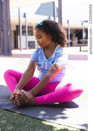 Biracial girl practices yoga outdoors at school 116309088