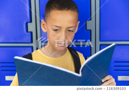 In a school, a young biracial boy stands before a blue locker background 116309103