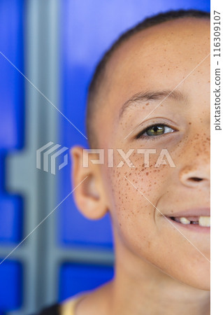 Biracial boy smiles against a blue background in school 116309107