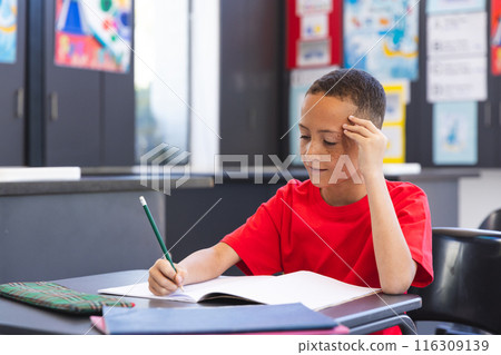 Biracial boy focuses on his schoolwork in a classroom at school Biracial boy focuses on his schoolwork in a classroom at school 116309139