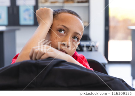 Biracial boy looks thoughtful in a classroom setting at school 116309155