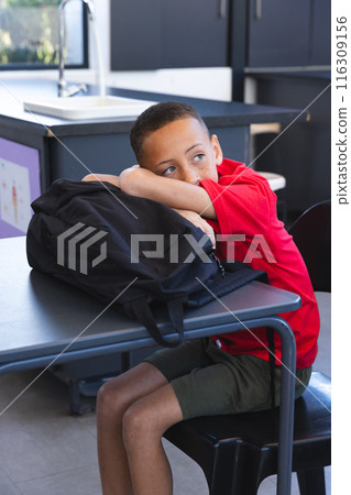 Biracial boy sits at a school desk, looking thoughtful Biracial boy sits at a school desk, looking thoughtful 116309156