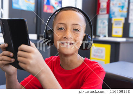 Biracial boy enjoys music on his tablet in the school classroom using a tablet 116309158