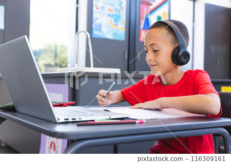Biracial boy studies intently in a school classroom using a laptop, with copy space Biracial boy studies intently in a school classroom using a laptop, with copy space 116309161