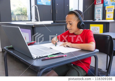 Biracial boy studies intently in a school classroom using a laptop, with copy space Biracial boy studies intently in a school classroom using a laptop, with copy space 116309166