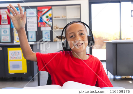 Biracial boy raises his hand in a classroom setting at school 116309176