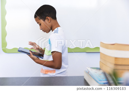 Biracial boy focused on reading a tablet at school Biracial boy focused on reading a tablet at school 116309183