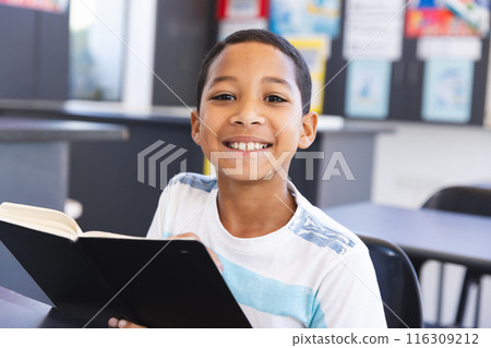 Biracial boy reading a book in the classroom at school Biracial boy reading a book in the classroom at school 116309212