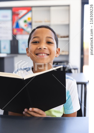 Biracial boy reading a book in a classroom at school, with copy space Biracial boy reading a book in a classroom at school, with copy space 116309226