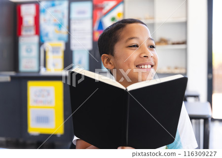 Biracial boy enjoys reading a book in the classroom at school 116309227