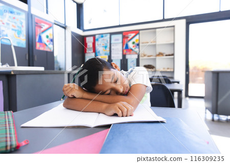 Exhausted biracial boy rests on desk during studies in bright classroom. Exhausted biracial boy rests on desk during studies in bright classroom. 116309235