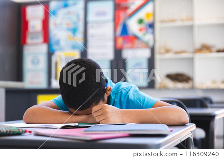 In a school classroom, a young Asian student rests his head on his arms In a school classroom, a young Asian student rests his head on his arms 116309240
