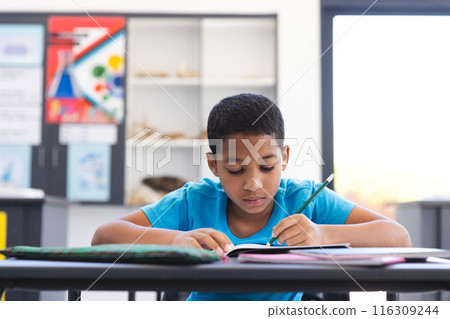 Biracial boy focused on his schoolwork in the classroom at school 116309244