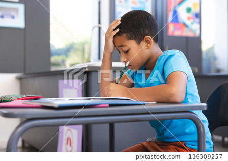 Biracial boy focused on schoolwork in the classroom at school Biracial boy focused on schoolwork in the classroom at school 116309257