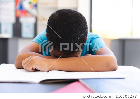 Biracial boy studying in a classroom, head resting on arms at school Biracial boy studying in a classroom, head resting on arms at school 116309258