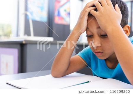 Biracial boy studying hard in the classroom at school, with copy space 116309260