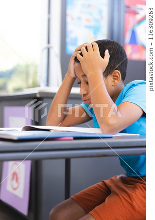 Biracial boy looks frustrated with schoolwork in the classroom at school 116309263
