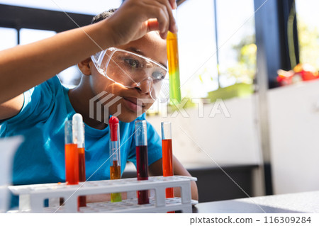 Biracial boy engaged in a science experiment at school in the classroom with copy space 116309284