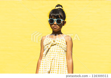 Biracial girl wearing sunglasses and a sundress poses confidently outdoors 116309311