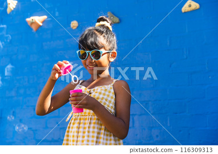 Biracial girl wearing sunglasses and a sundress enjoys outdoor playtime, with copy space 116309313