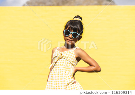 Biracial girl wearing sunglasses and a sundress poses confidently outdoors 116309314