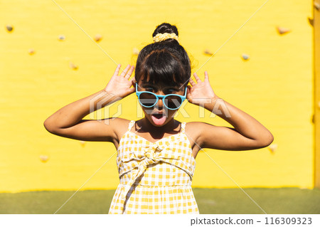 Biracial girl wearing sunglasses and a sundress makes a playful face outdoors Biracial girl wearing sunglasses and a sundress makes a playful face outdoors 116309323