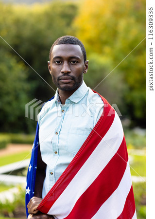 Portrait of serious african american man covered with flag of usa in garden Portrait of serious african american man covered with flag of usa in garden 116309336