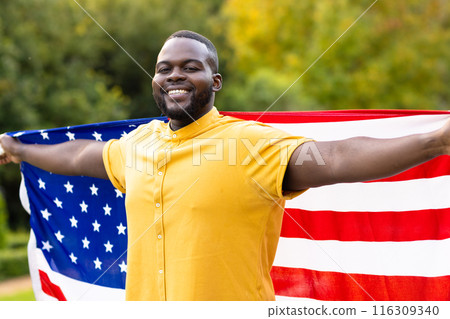 Portrait of happy african american man covered with flag of usa with arms wide in garden Portrait of happy african american man covered with flag of usa with arms wide in garden 116309340
