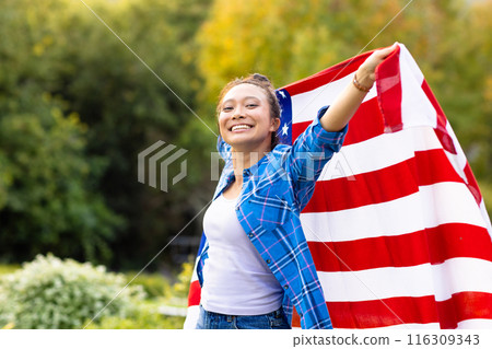 Portrait of happy asian woman covered with flag of usa in garden 116309343